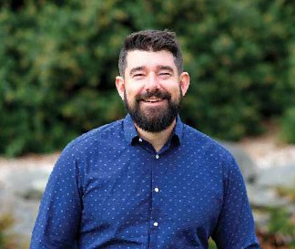 John Scott smiling outdoors in a blue shirt